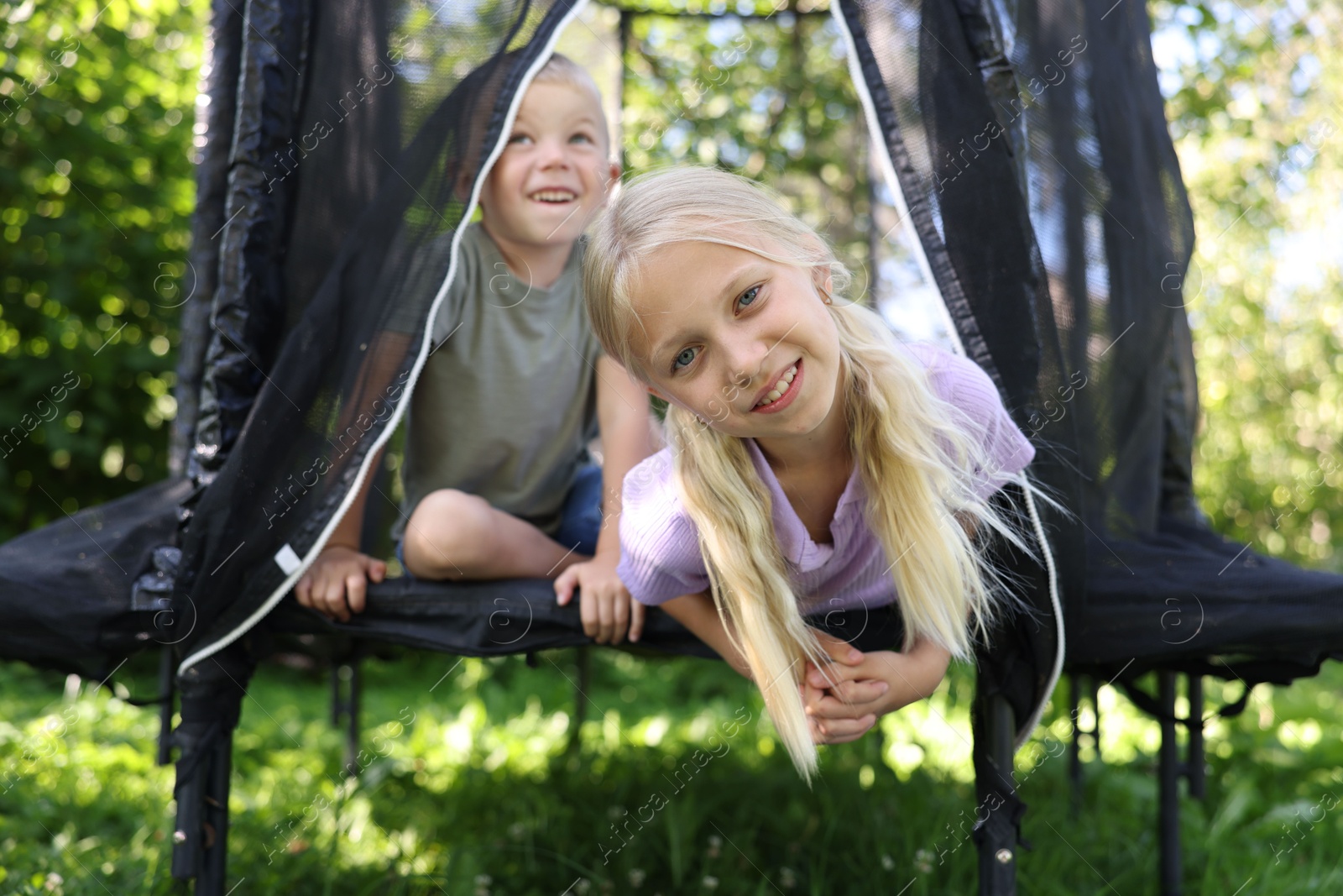 Happy little girl and her friends having fun on black trampoline outdoors Photo of Happy little girl and her friends having fun on black trampoline outdoors