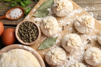 Photo of Uncooked khinkalis (dumplings) with peppercorns, flour, parsley and bay leaves on wooden table, flat lay