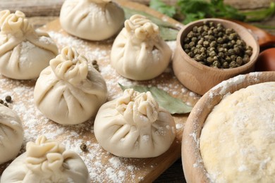Photo of Uncooked khinkalis (dumplings) with peppercorns, flour and bay leaves on wooden table, closeup