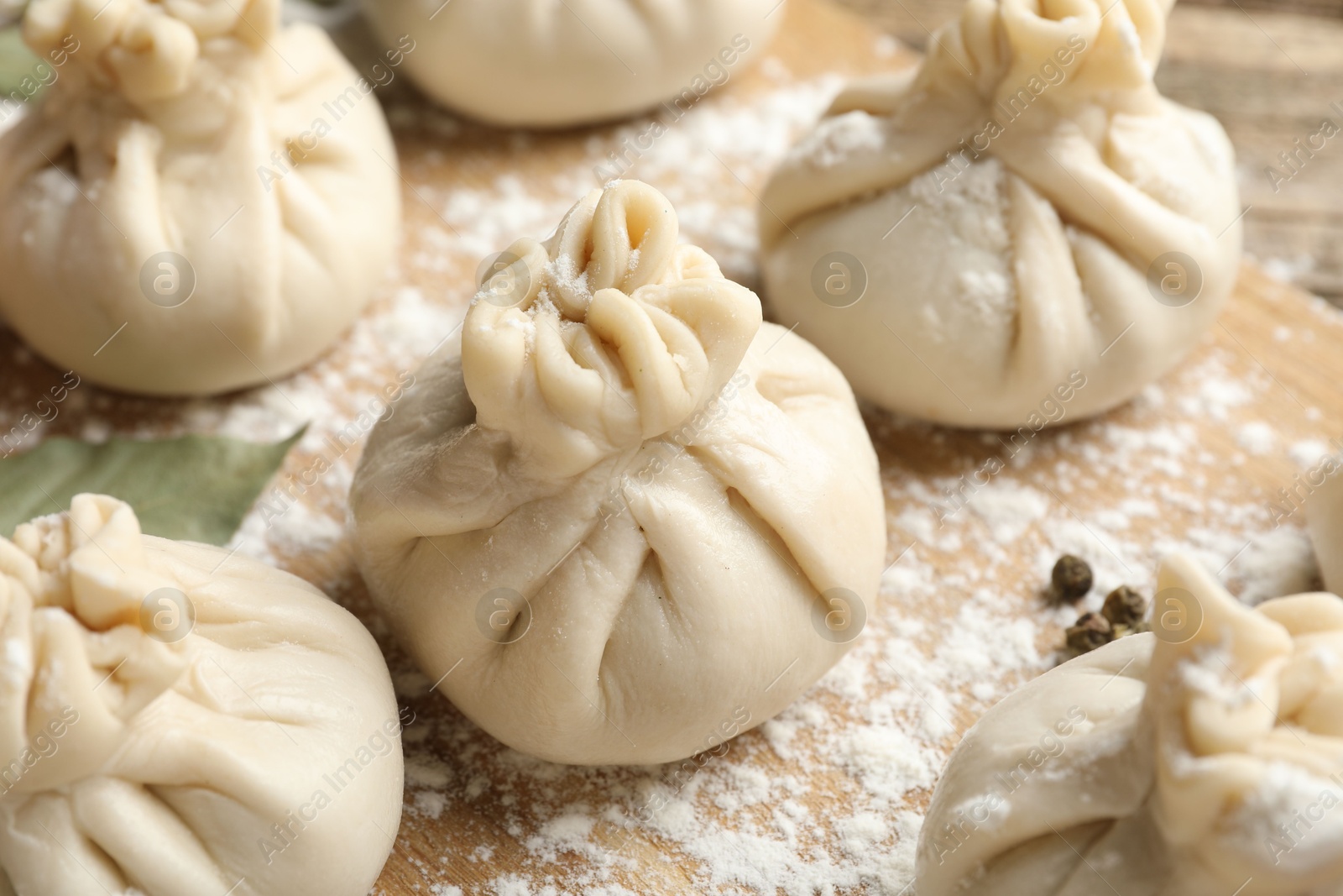 Uncooked khinkalis (dumplings) with flour on wooden table, closeup Photo of Uncooked khinkalis (dumplings) with flour on wooden table, closeup