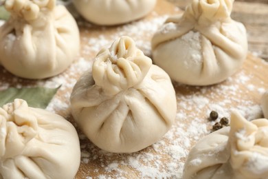 Photo of Uncooked khinkalis (dumplings) with flour on wooden table, closeup