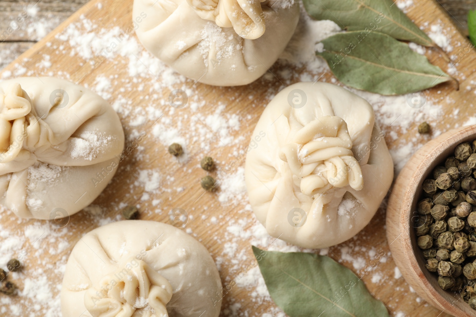 Uncooked khinkalis (dumplings) with peppercorns, flour and bay leaves on wooden table, flat lay Photo of Uncooked khinkalis (dumplings) with peppercorns, flour and bay leaves on wooden table, flat lay