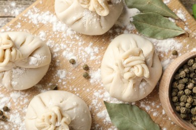 Photo of Uncooked khinkalis (dumplings) with peppercorns, flour and bay leaves on wooden table, flat lay
