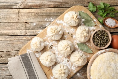 Photo of Uncooked khinkalis (dumplings) with peppercorns, flour, parsley and bay leaves on wooden table, flat lay