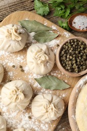 Photo of Uncooked khinkalis (dumplings) with peppercorns, flour, parsley and bay leaves on wooden table, flat lay