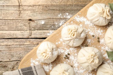 Photo of Uncooked khinkalis (dumplings) with peppercorns, flour and bay leaves on wooden table, top view. Space for text