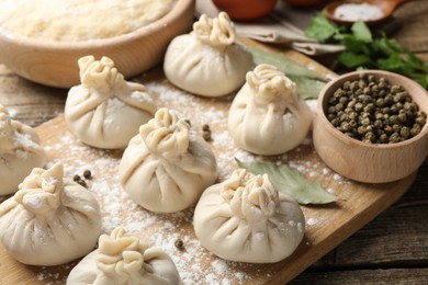 Photo of Uncooked khinkalis (dumplings) with peppercorns, flour and bay leaves on wooden table, closeup