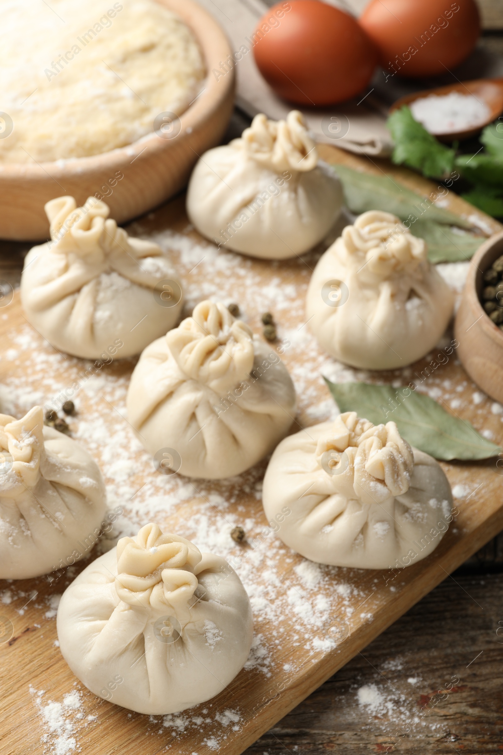 Photo of Uncooked khinkalis (dumplings) with peppercorns, flour and bay leaves on wooden table, closeup