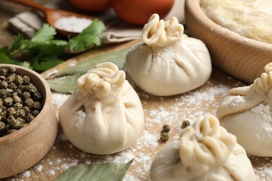 Photo of Uncooked khinkalis (dumplings) with peppercorns, flour and bay leaves on wooden table, closeup