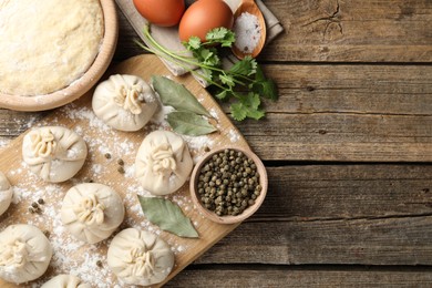 Photo of Uncooked khinkalis (dumplings) with peppercorns, flour and bay leaves on wooden table, top view. Space for text