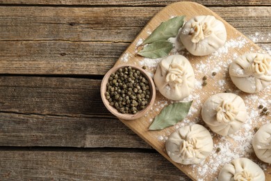 Photo of Uncooked khinkalis (dumplings) with peppercorns, flour and bay leaves on wooden table, top view. Space for text