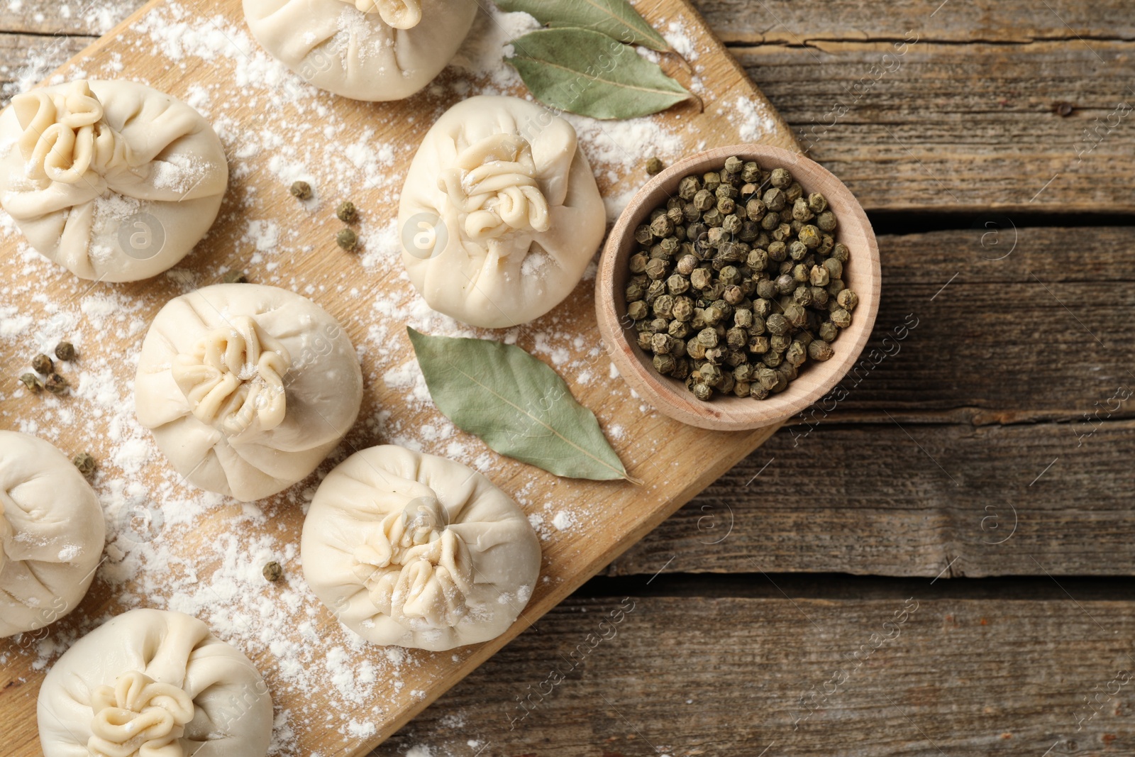 Photo of Uncooked khinkalis (dumplings) with peppercorns, flour and bay leaves on wooden table, top view