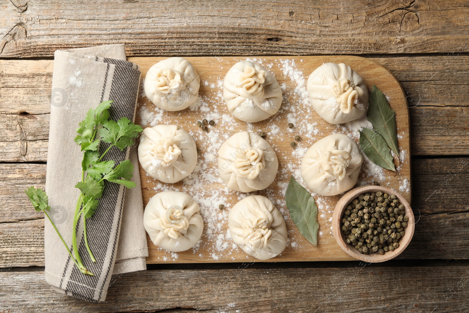 Photo of Uncooked khinkalis (dumplings) with peppercorns, flour, parsley and bay leaves on wooden table, flat lay