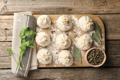 Photo of Uncooked khinkalis (dumplings) with peppercorns, flour, parsley and bay leaves on wooden table, flat lay