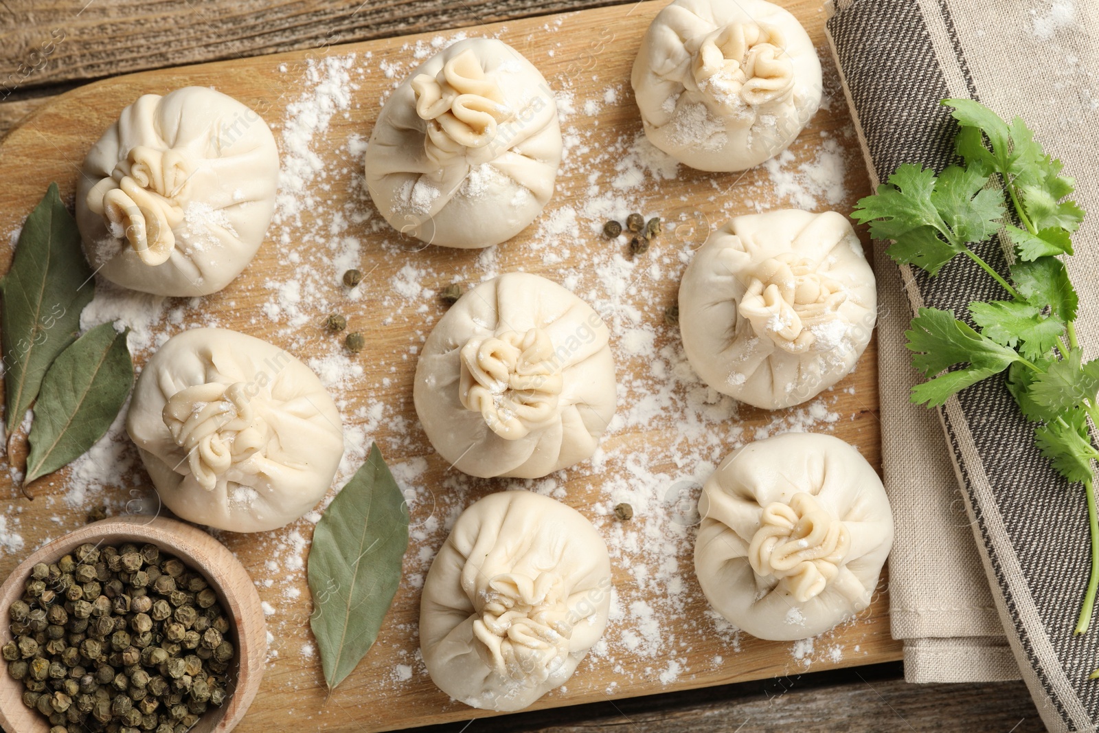 Photo of Uncooked khinkalis (dumplings) with peppercorns, flour, parsley and bay leaves on wooden table, flat lay