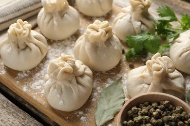 Photo of Uncooked khinkalis (dumplings) with peppercorns, flour and bay leaves on wooden table, closeup