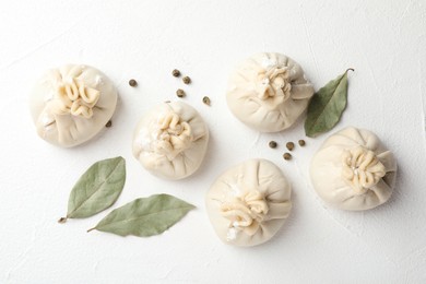 Photo of Uncooked khinkalis (dumplings) with peppercorns and bay leaves on white table, flat lay