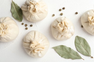 Photo of Uncooked khinkalis (dumplings) with peppercorns and bay leaves on white table, flat lay