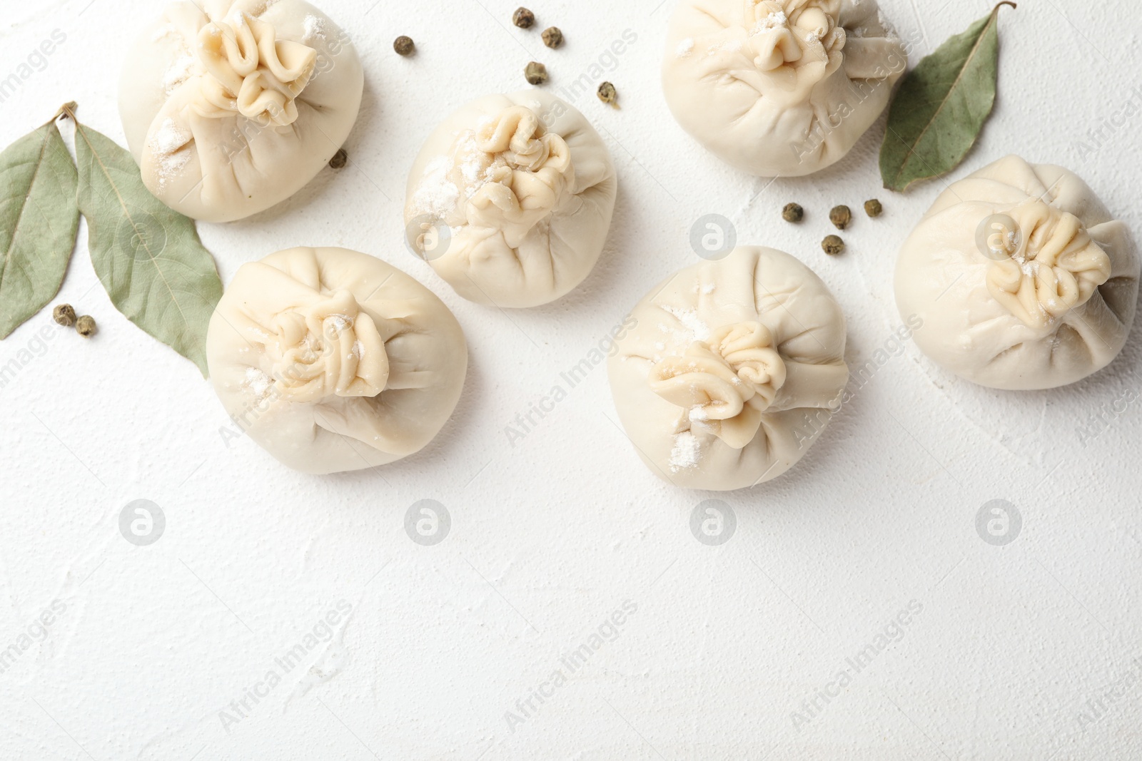 Photo of Uncooked khinkalis (dumplings) with peppercorns and bay leaves on white table, flat lay. Space for text