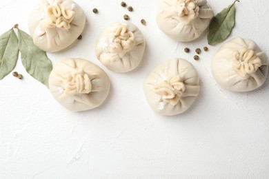 Photo of Uncooked khinkalis (dumplings) with peppercorns and bay leaves on white table, flat lay. Space for text