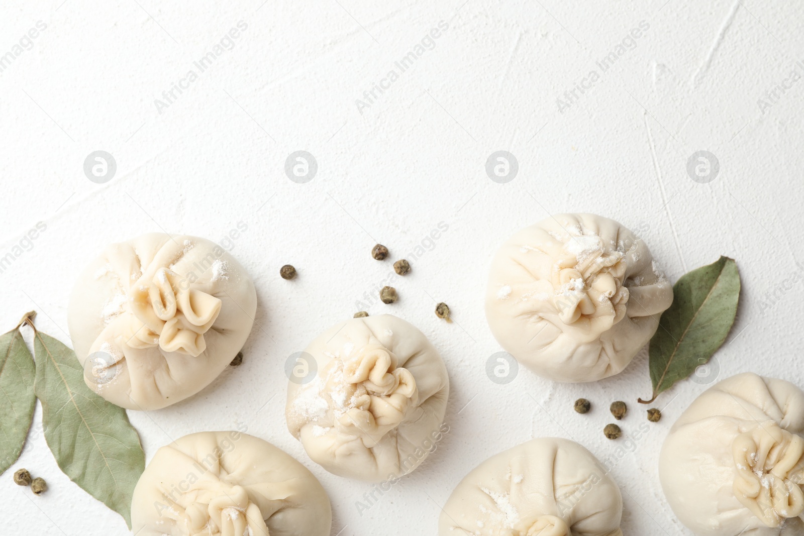 Photo of Uncooked khinkalis (dumplings) with peppercorns and bay leaves on white table, flat lay. Space for text