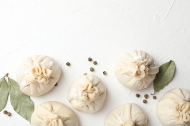 Photo of Uncooked khinkalis (dumplings) with peppercorns and bay leaves on white table, flat lay. Space for text