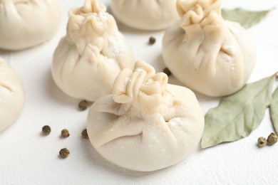 Photo of Uncooked khinkalis (dumplings) with peppercorns and bay leaves on white table, closeup
