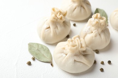 Photo of Uncooked khinkalis (dumplings) with peppercorns and bay leaves on white table, closeup
