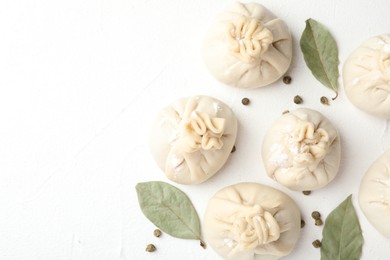 Photo of Uncooked khinkalis (dumplings) with peppercorns and bay leaves on white table, flat lay. Space for text