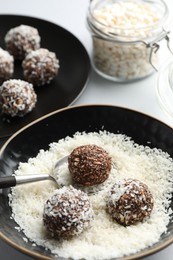 Photo of Making tasty chocolate candies with nuts and coconut flakes at white table, closeup