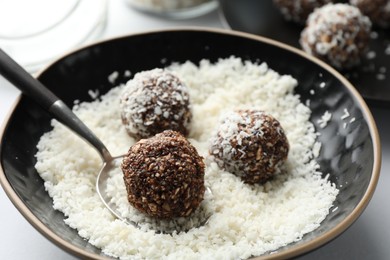 Photo of Making tasty chocolate candies with nuts and coconut flakes at white table, closeup