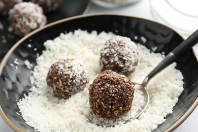 Photo of Making tasty chocolate candies with nuts and coconut flakes at white table, closeup