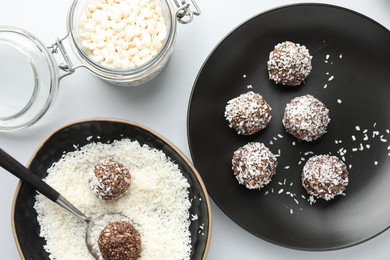 Photo of Making tasty chocolate candies with nuts and coconut flakes at white table, flat lay