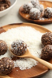 Photo of Making tasty chocolate candies with nuts and coconut flakes at light table, closeup