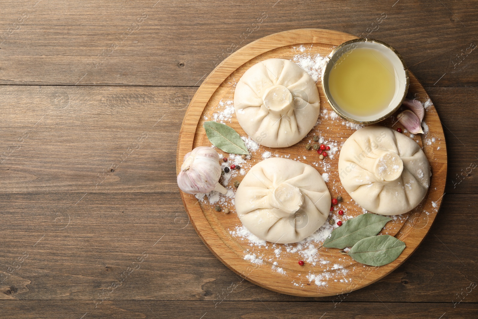 Photo of Uncooked khinkalis (dumplings) with peppercorns, flour and bay leaves on wooden table, top view. Space for text