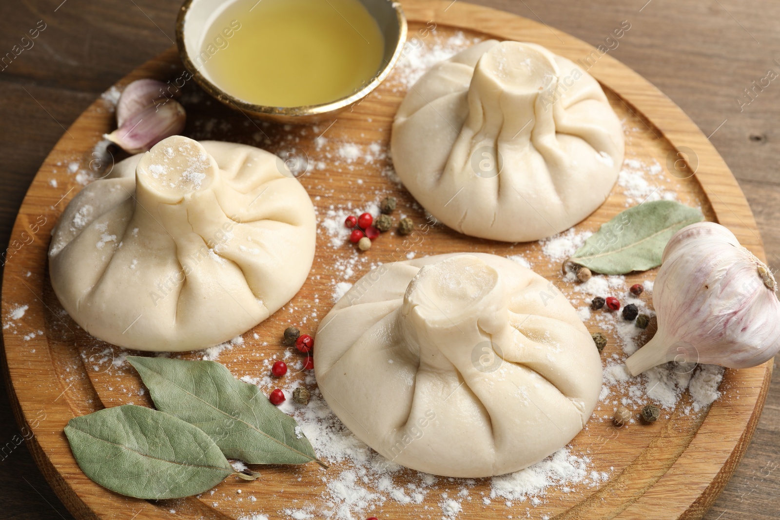 Photo of Uncooked khinkalis (dumplings) with peppercorns, flour and bay leaves on wooden table, closeup