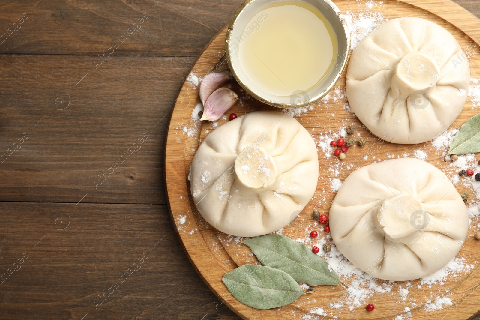 Photo of Uncooked khinkalis (dumplings) with peppercorns, flour and bay leaves on wooden table, top view. Space for text