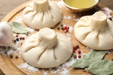 Photo of Uncooked khinkalis (dumplings) with peppercorns, flour and bay leaves on wooden table, closeup