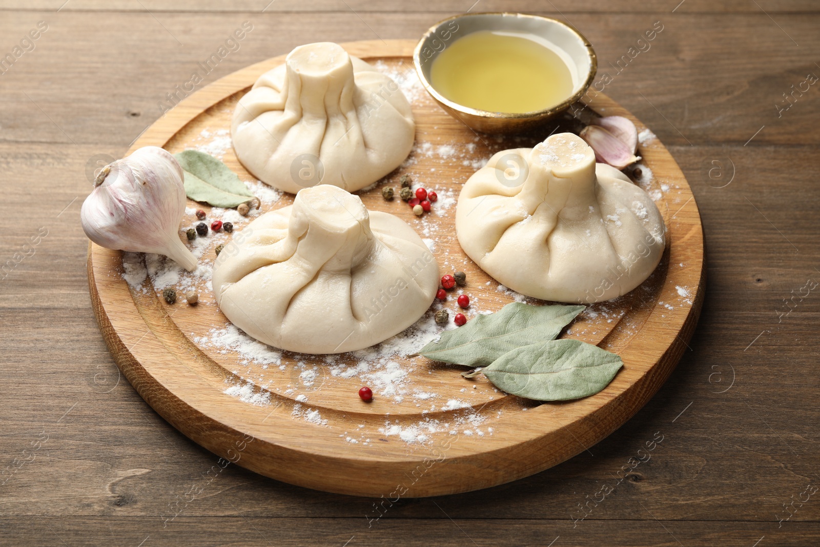 Photo of Uncooked khinkalis (dumplings) with peppercorns, flour and bay leaves on wooden table