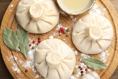 Photo of Uncooked khinkalis (dumplings) with peppercorns, flour and bay leaves on wooden table, top view