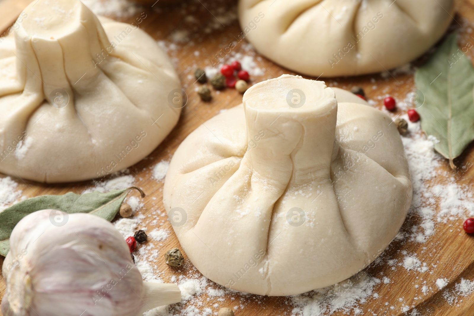 Photo of Uncooked khinkalis (dumplings) with peppercorns, flour and bay leaves on wooden table, closeup