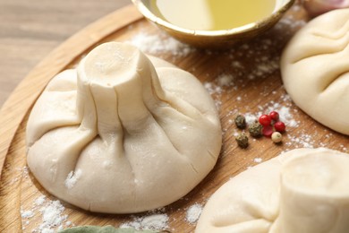 Photo of Uncooked khinkalis (dumplings) with peppercorns and flour on wooden table, closeup