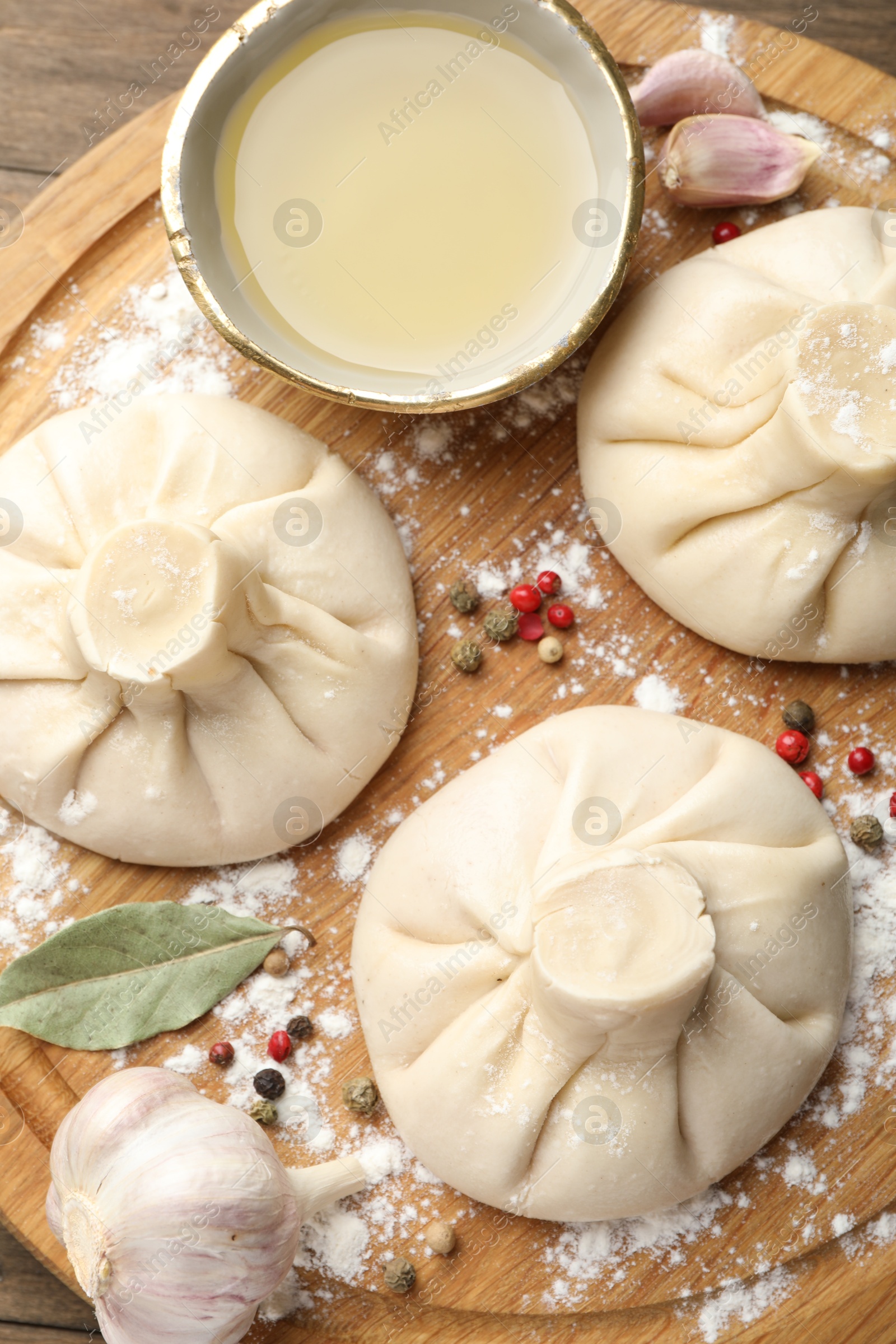 Photo of Uncooked khinkalis (dumplings) with peppercorns, flour and bay leaves on wooden table, top view
