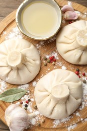 Photo of Uncooked khinkalis (dumplings) with peppercorns, flour and bay leaves on wooden table, top view