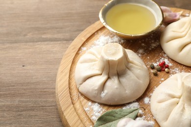 Photo of Uncooked khinkalis (dumplings) with peppercorns, flour and bay leaves on wooden table, closeup. Space for text