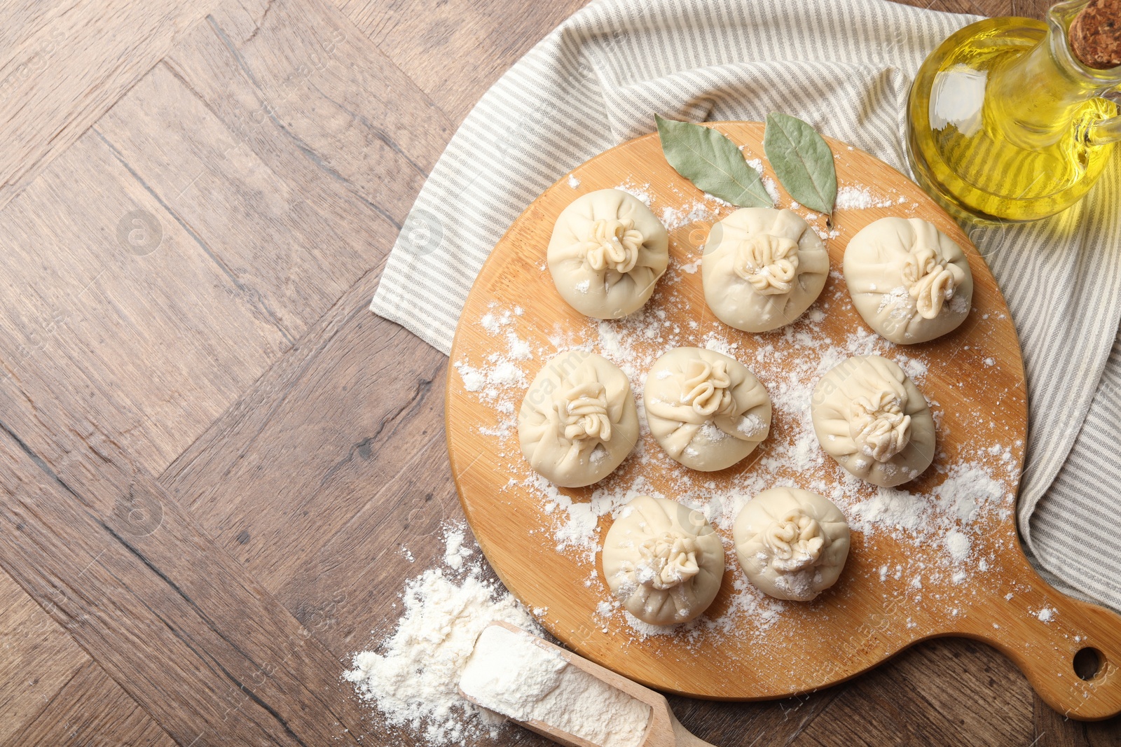 Photo of Uncooked khinkalis (dumplings) with flour, oil and bay leaves on wooden table, top view. Space for text