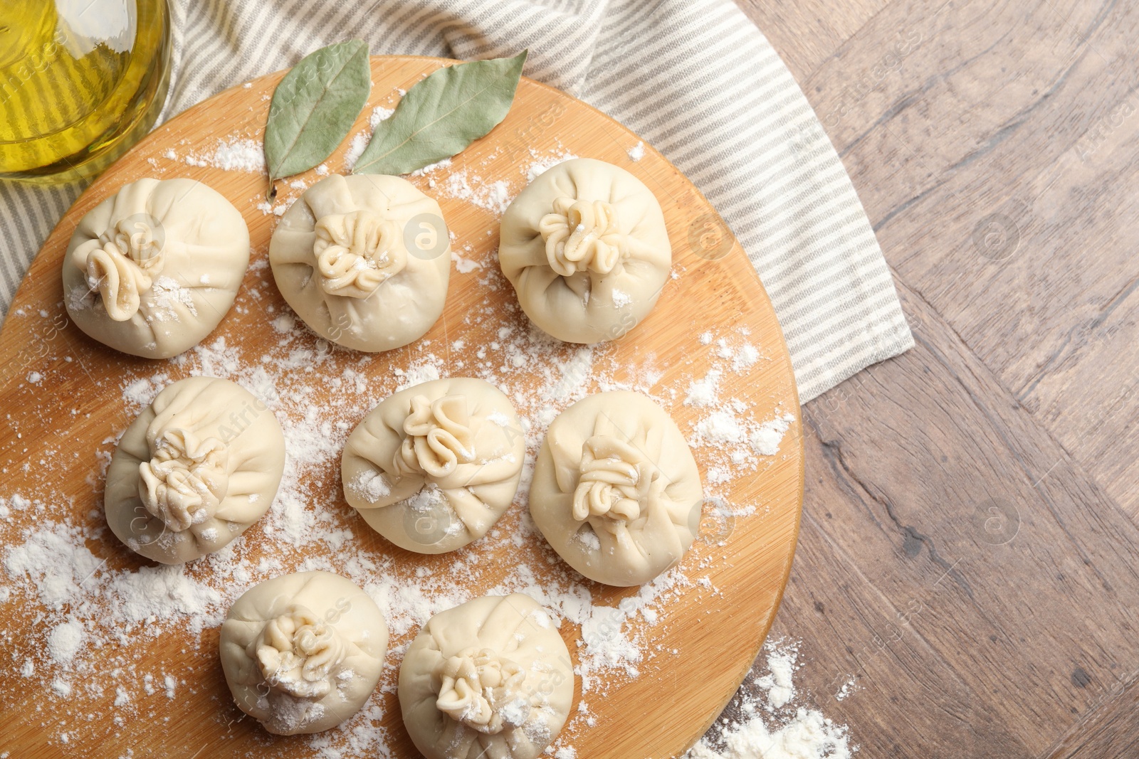 Photo of Uncooked khinkalis (dumplings) with flour, oil and bay leaves on wooden table, top view. Space for text