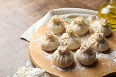 Photo of Uncooked khinkalis (dumplings) with flour, oil and bay leaves on wooden table, closeup