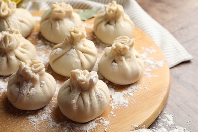 Photo of Uncooked khinkalis (dumplings) with flour on wooden table, closeup