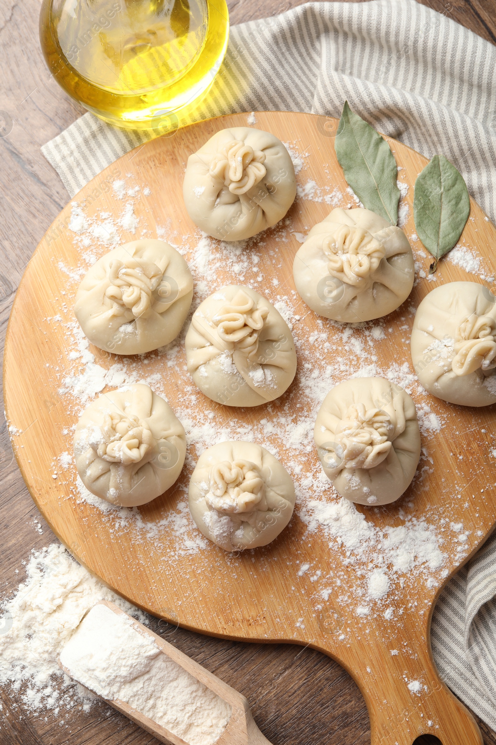 Photo of Uncooked khinkalis (dumplings) with flour, oil and bay leaves on wooden table, top view